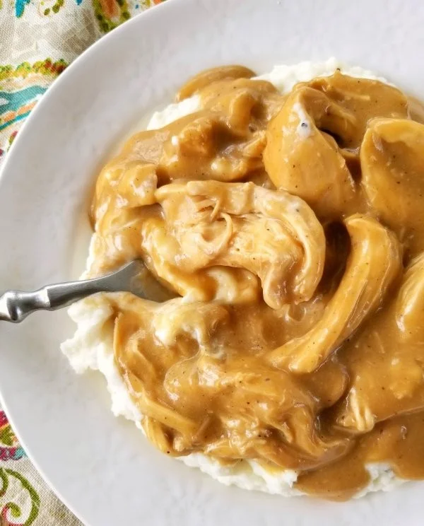Crock Pot chicken and gravy served on a plate with fresh herbs