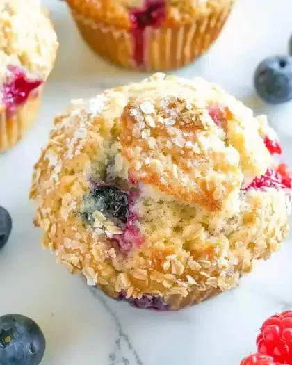 Freshly baked mixed berry muffins with a variety of berries on a wooden table